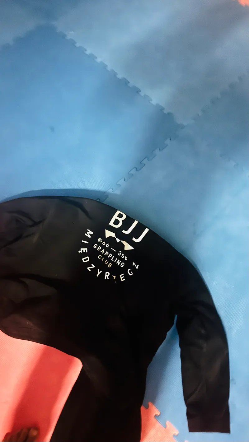 Czarne kimono z białym logo klubu na niebieskiej macie