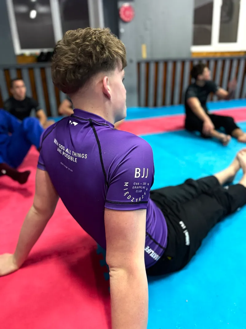 Zawodnik w fioletowym rashguardzie z logo klubu na rękawie