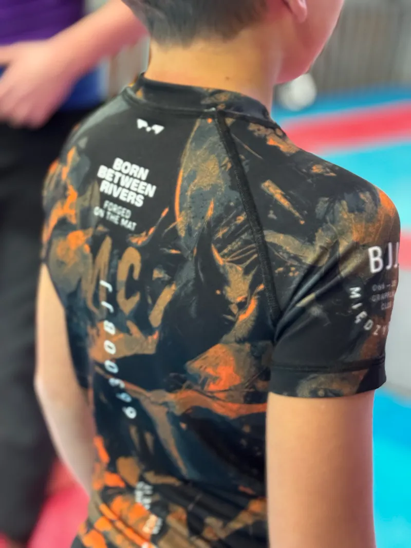 Młody zawodnik w czarno-pomarańczowym rashguardzie klubu